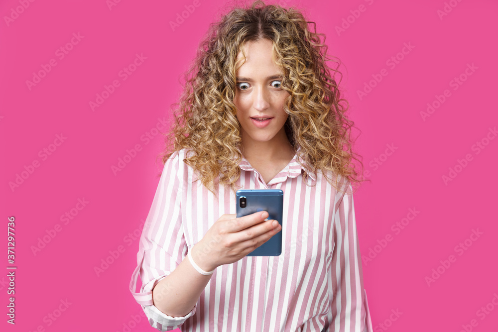 A fashionable woman in a striped shirt, holds a mobile phone, gasps in surprise, reads amazing news. A fashionable woman in a striped shirt, holds a mobile phone, gasps in surprise, reads amazing news.
