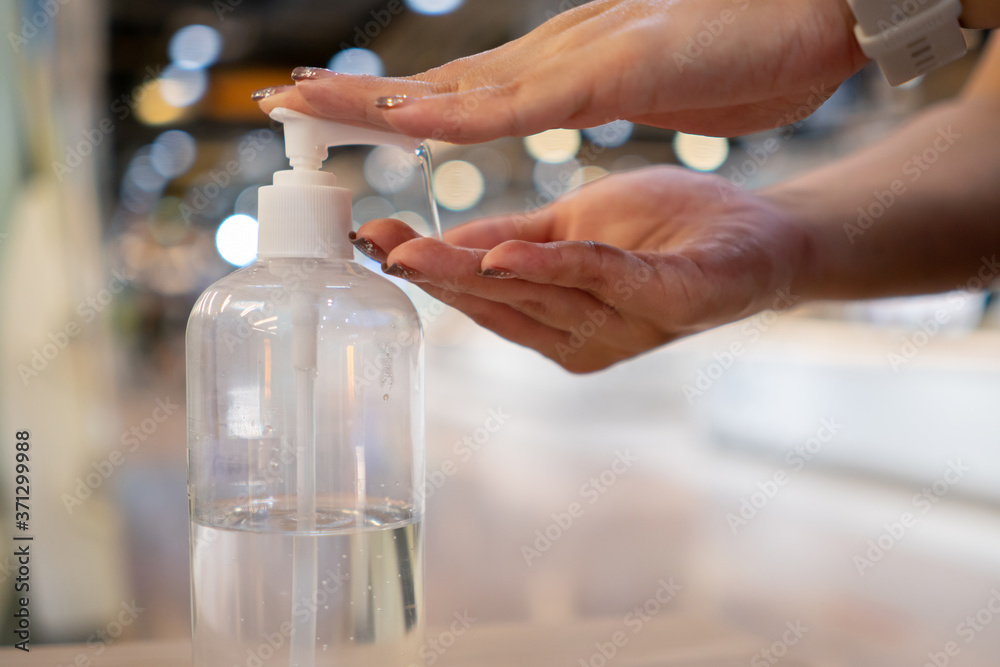 Woman washes her hands with clear alcohol gel bottle before entering the supermarket.