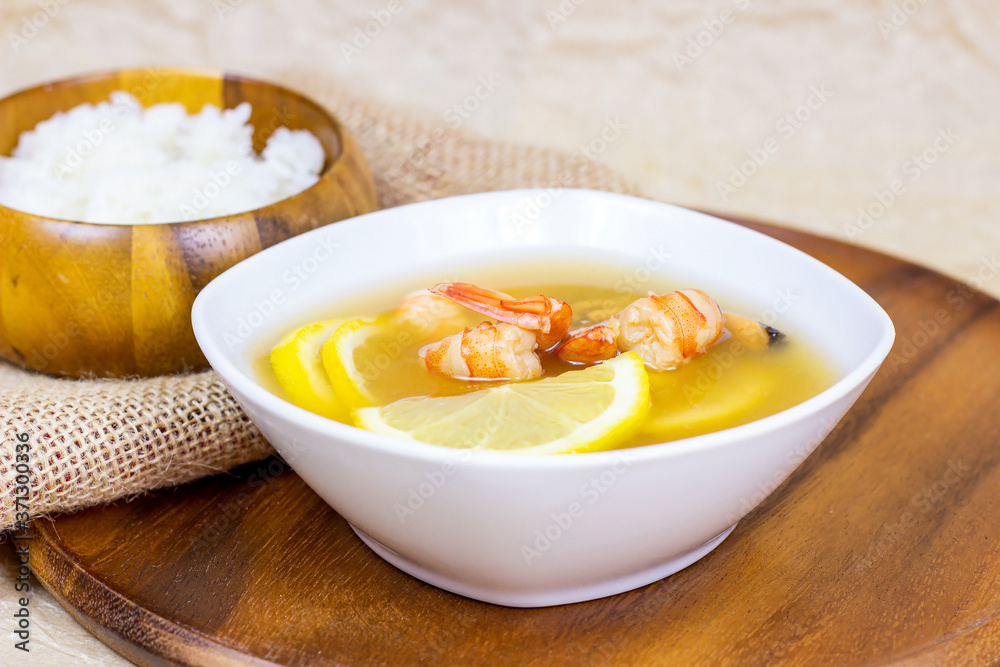 White bowl with traditional light spicy thai cuisine tom yam soup with shrimps, seafood and lemon on wooden board background. White bowl with traditional light spicy thai cuisine tom yam soup with shrimps, seafood and lemon on wooden board background.