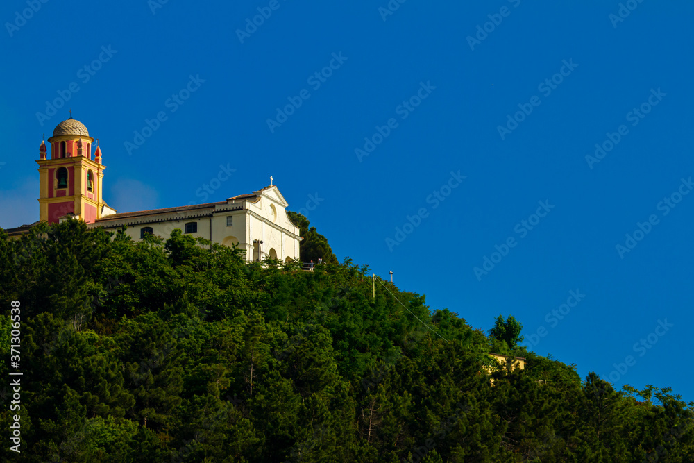 A small catholic church with a vibrant bell tower on a mountain covered with trees. This is a remote location in Liguria, Italy.