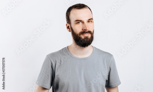 Wallpaper Mural A handsome brutal brunette man with a beard in a gray shirt smiles and looks at the camera. Place for advertising on a gray background. Torontodigital.ca