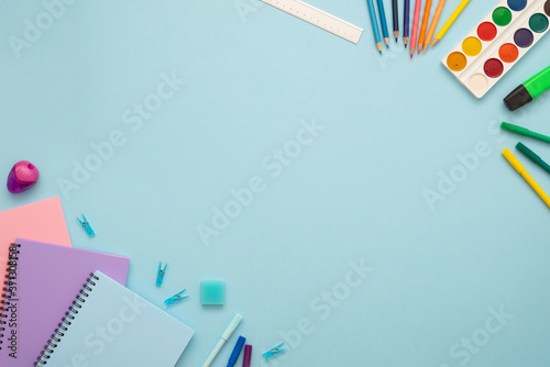 Top view of blue, pink and purple notebooks, pins, eraser, felt tip pens, color pencils, ruler, marker and watercolor. School stationery set on the blue background. Copy space. 