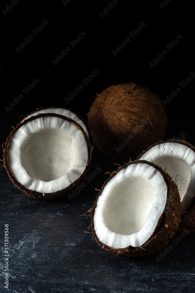 Coconut on a black background. Chopped coconut. Several parts. Stone surface. Fresh coconut. White pulp.