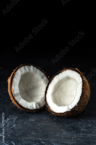 Coconut on a black background. Chopped coconut. Several parts. Stone surface. Fresh coconut. White pulp.