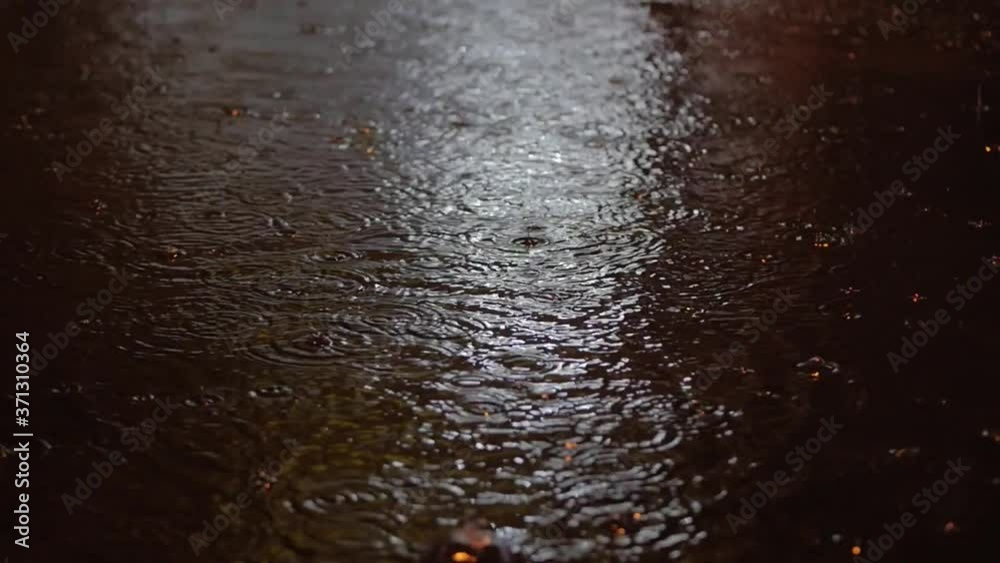 At night Close-up drops of summer or autumn rain fall on the asphalt in the city, turning into a large puddle, flooding the street. Floods are the rainy season and heavy rains. Raindrops are falling. At night Close-up drops of summer or autumn rain fall on the asphalt in the city, turning into a large puddle, flooding the street. Floods are the rainy season and heavy rains. Raindrops are falling.