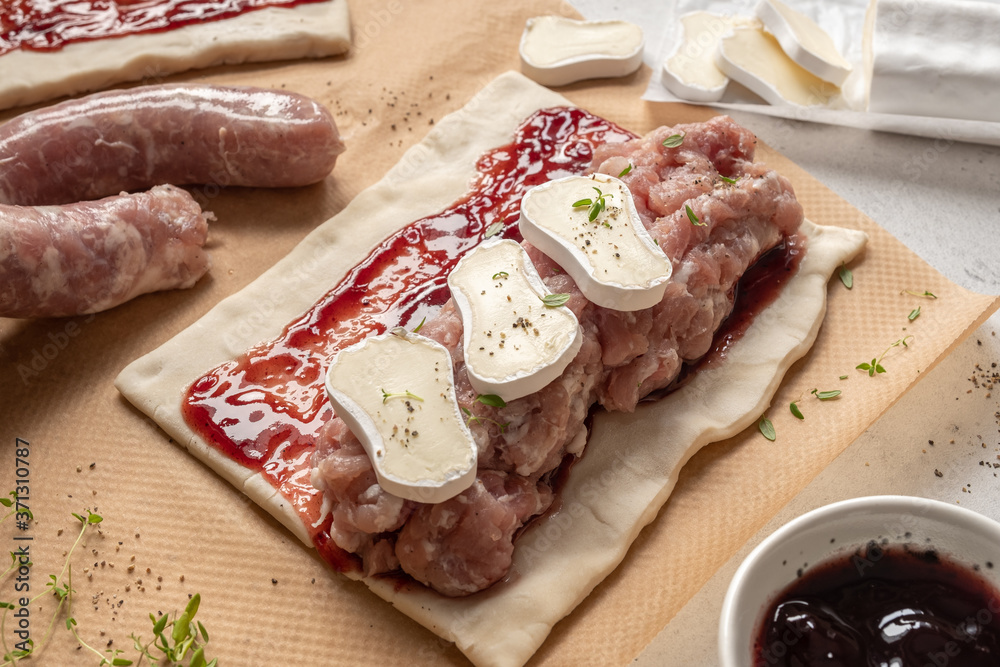 Raw prepared pork turkey sausage rolls with brie cheese and cranberry sauce in puff pastry Raw prepared pork turkey sausage rolls with brie cheese and cranberry sauce in puff pastry