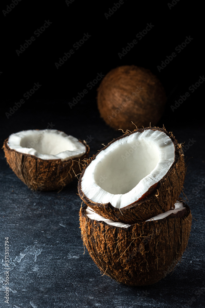 Coconut on a black background. Chopped coconut. Several parts. Stone surface. Fresh coconut. White pulp. Coconut on a black background. Chopped coconut. Several parts. Stone surface. Fresh coconut. White pulp.