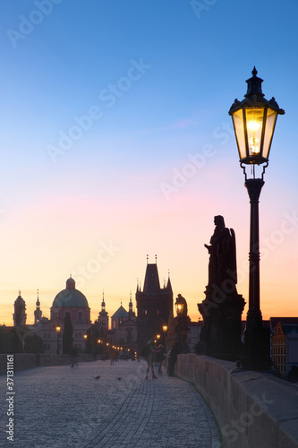 Charles Bridge in twilight. Historic street light, silhouette of Bridge Tower and saint sculptures in Prague, Czech Republic.