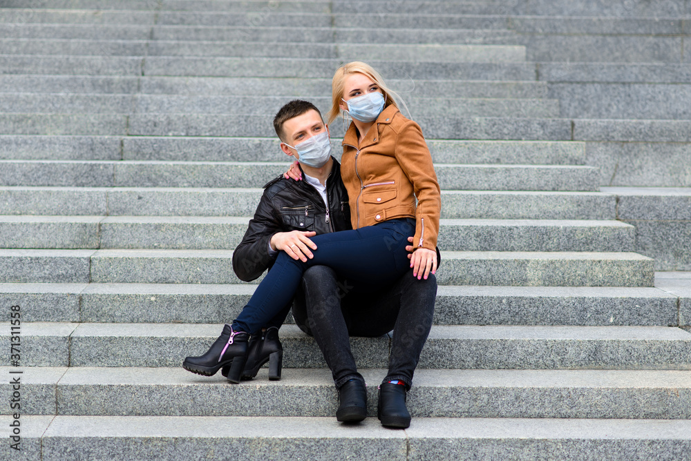 Couple in protective masks have a walk outdoors in the city near business building at quarantine time. Conception of coronavirus. Couple in protective masks have a walk outdoors in the city near business building at quarantine time. Conception of coronavirus.