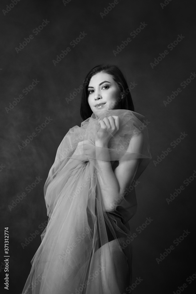 A beautiful, delicate girl with dark hair, wrapped in a tulle cloth.