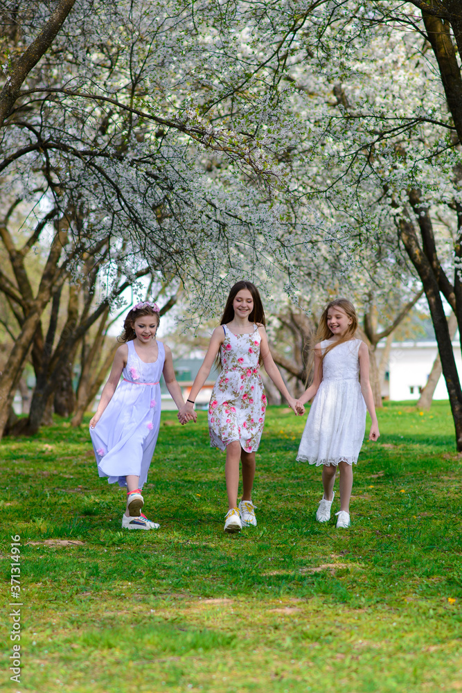Three adorable girls in dresses hold hands in the garden, park. Three adorable girls in dresses hold hands in the garden, park.