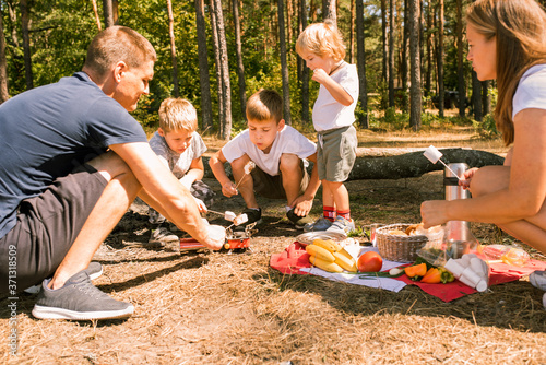 Three little boys staged a halt with a tent and a campfire in the woods in summer sunny day.campfire food