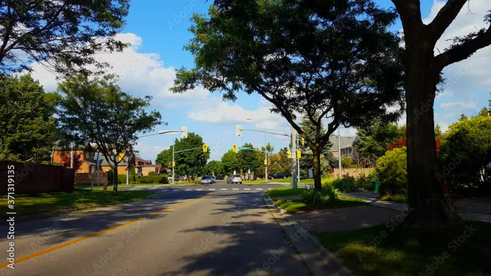 Bicyclist Rides Through City Suburb Light Intersection in Summer. Person on Bike Driving Urban Suburban Vehicles Drive Through Traffic Light Intersection During Day. Bicyclist Rides Through City Suburb Light Intersection in Summer. Person on Bike Driving Urban Suburban Vehicles Drive Through Traffic Light Intersection During Day.