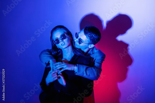 Couple of girl lovers and guy cuddling in red blue neon lights