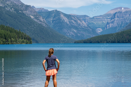 Attractive young woman with back facing camera looks at the scenery of Bowman Lake in Glacier National Park Montana