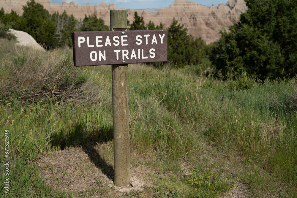 Sign reminding hikers to Please Stay on Trails, in Badlands National Park, preventing falls and other mishaps Sign reminding hikers to Please Stay on Trails, in Badlands National Park, preventing falls and other mishaps