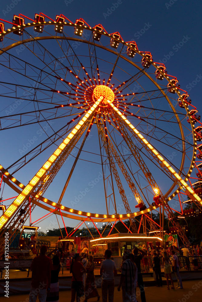 Odessa, Ukraine - June 4, 2011: Ferris wheel in the evening. Cabins of a Ferris wheel illuminated with colored lamps. People have fun on rides in city Park. Odessa, Ukraine - June 4, 2011: Ferris wheel in the evening. Cabins of a Ferris wheel illuminated with colored lamps. People have fun on rides in city Park.