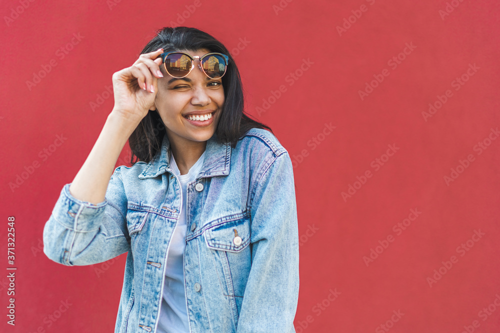 Half-length portrait of cute casually dressed dark skinned girl posing against red wall winking and smiling Half-length portrait of cute casually dressed dark skinned girl posing against red wall winking and smiling