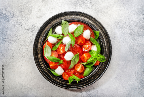 Tasty caprese salad with ripe red tomatoes and mozzarella cheese with fresh green basil leaves. Italian food. Top view