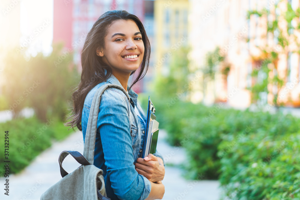 Half-length portrait of beautiful casually dressed student girl with charming smile posing outdoors with a backpack and pile of books and tablet in hands Half-length portrait of beautiful casually dressed student girl with charming smile posing outdoors with a backpack and pile of books and tablet in hands