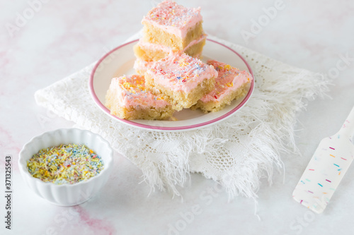 A pile of keto sugar cookie bars ready for eating with a small bowl of coconut sprinkles. photo