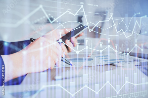 Double exposure of man's hands holding and using a phone and financial graph drawing. Analysis concept.