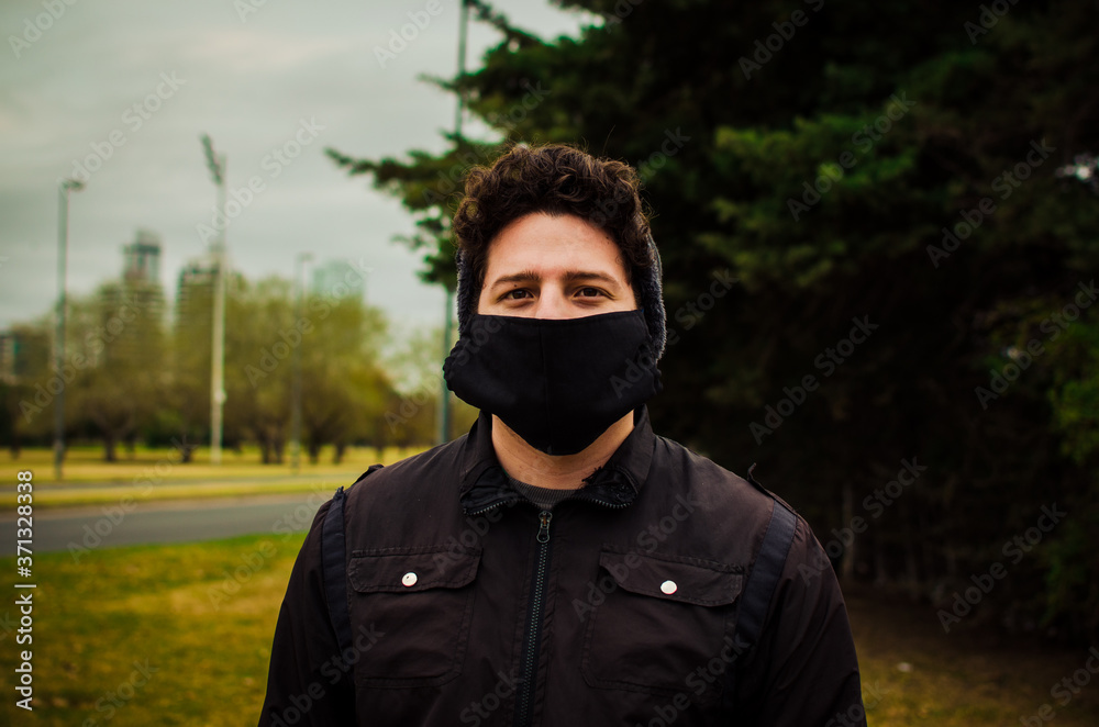 Hombre joven vestido de negro usando mascarilla facial contra el coronavirus. Pandemia. COVID-19.