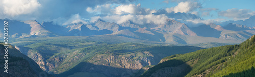 Mountain range, panoramic view. Peaks in the clouds, evening light.