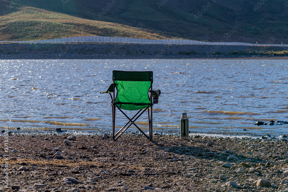 Camping area on a lake in mountainous terrain. A camp chair and a tea thermos