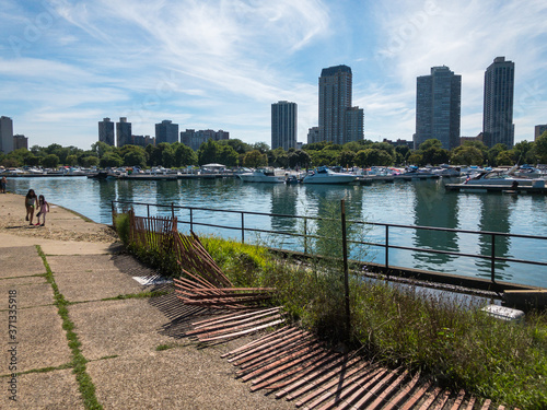 girls wearing masks walking next to Diversey Harbor with broken fence and boats and skyline of Chicago photo