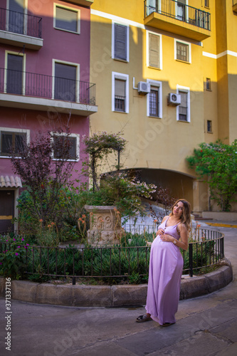 beautiful young pregnant girl in a purple dress stands in the old city © Bas