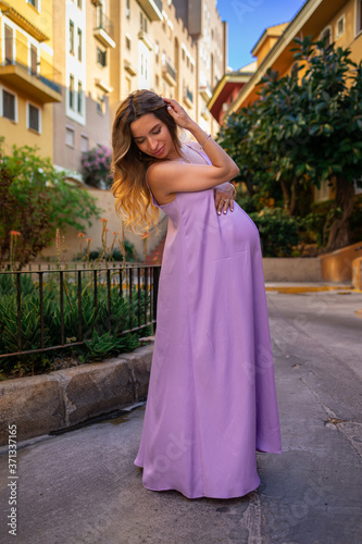 beautiful young pregnant girl in a purple dress stands in the old city
