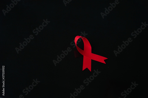 red ribbon as symbol of fighting cancer illness on wooden board with copy spacered ribbon as symbol of fighting cancer illness on black background with copy space photo