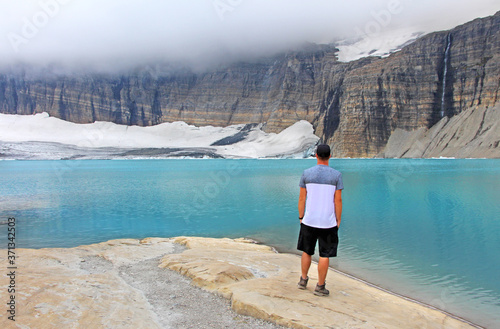 Grinnell Glacier trail in Montana, USA - Man, tourist and hiker is standing by beautiful turquoise lake and rocky mountains with glacier, enjoying the beautiful view. photo