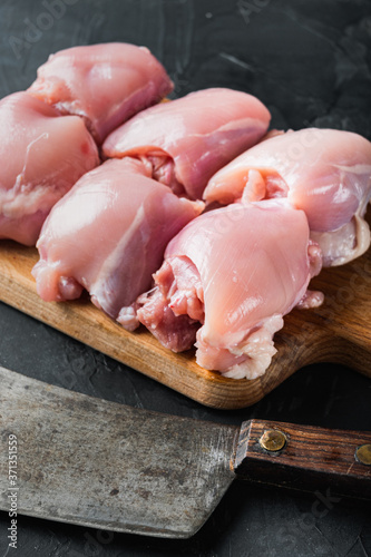 Fresh chicken thighs with meat cleaver, on black background