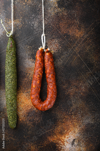 Dry cured chorizo and fuet salami sausages hanging on dark background, top view