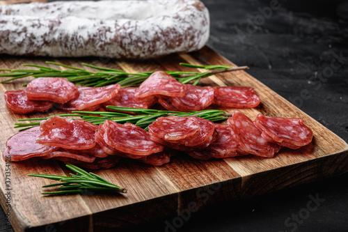 Fuet salami wurst cut in slices and whole sausage on black textured surface