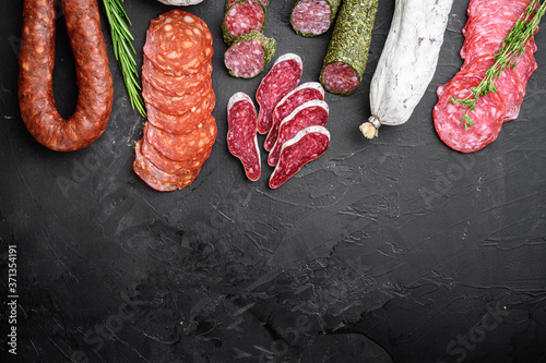 Set of dry cured salami, spanish sausages, slices and cuts on black background, top view with copy space photo