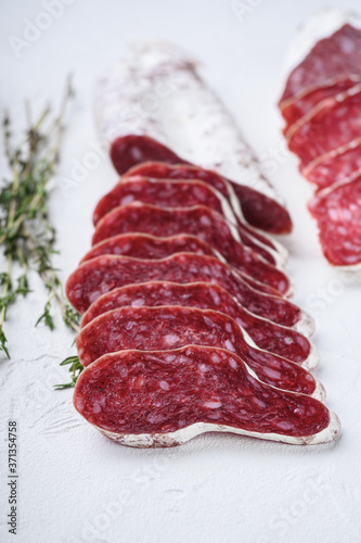 Variety of dry cured fuet and chorizosalami sausages, whole and sliced on white textured background