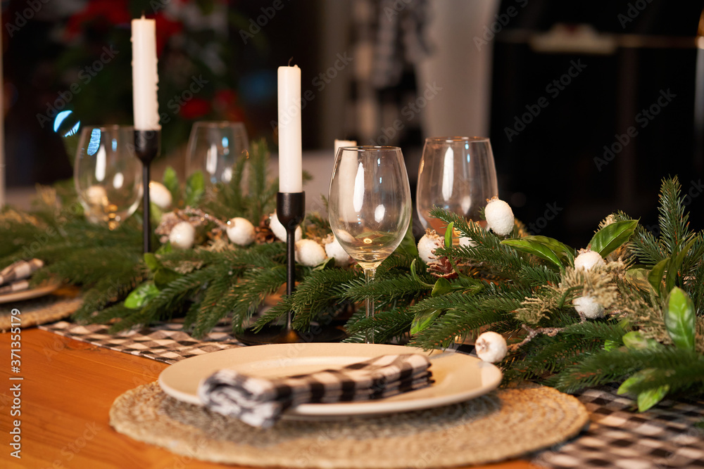 The festive Christmas table is decorated with branches of a Christmas tree, candles and garlands. Cozy home Christmas atmosphere.