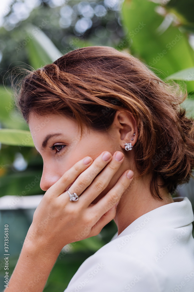 Fashion portrait of woman at tropical luxury villa wearing white stylish blazer, rings, earings on background of tropical leaves and swimming pool. Fashion portrait of woman at tropical luxury villa wearing white stylish blazer, rings, earings on background of tropical leaves and swimming pool.