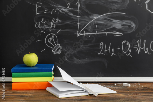 Books and apple on table against school blackboard