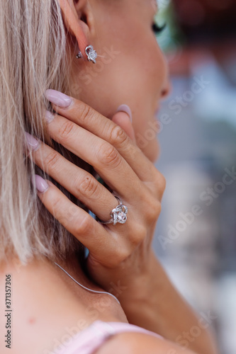 Close shot of rich luxury woman in dress hand and ear wearing earings and ring on finger. 