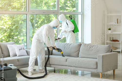 Workers in biohazard costume removing dirt from sofa in house