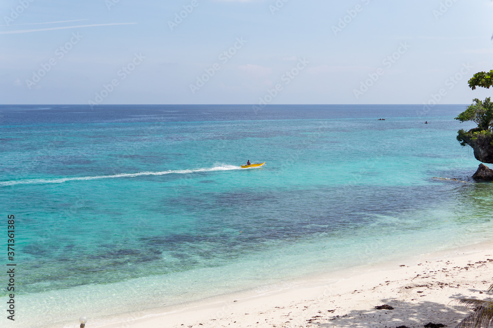 Unrecognizable Filipino man on small catamaran on paradise beach with turquoise water and white sand in Philippines