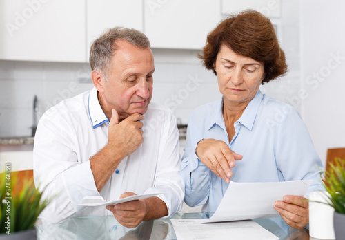 Unhappy mature family couple sitting at kitchen table with documents together © JackF