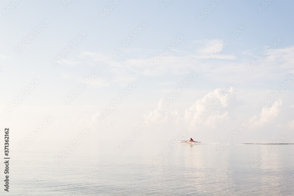 Unrecognizable Filipino man on small catamaran crossing the sea at high speed during sunrise with sea water indistinguishable from the sky