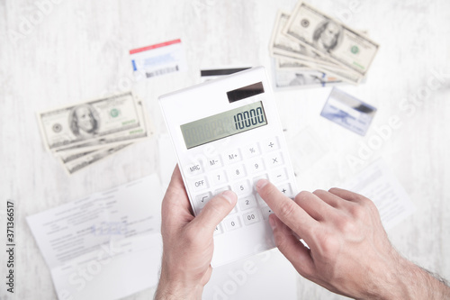 Man using calculator. Dollars, credit cards and document on the desk