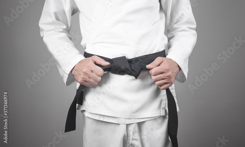 Caucasian man fixing his black belt. Karate