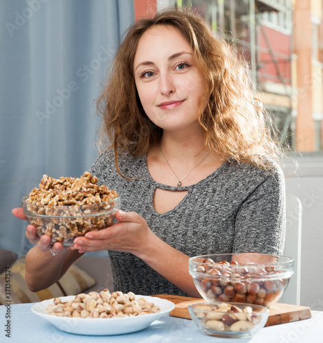 Young cheerful woman holding assorted nuts in glass bowls